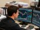 Focused Australian retail trader studying two or three CFD markets on multiple screens while a crowded assortment of other instruments fades into the background
